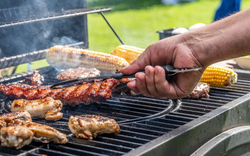 Close-up of man using tongs to take meat off on hot barbecue grill.