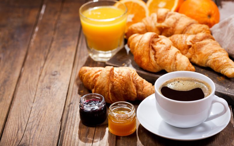breakfast with cup of coffee, croissants, orange juice and fruit jam on wooden table